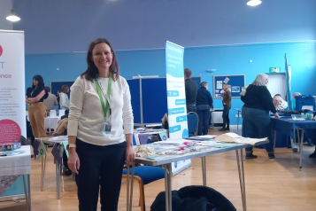 Our North Somerset Projects and Engagement Officer, Katie, standing in front of a table covered in Healthwatch North Somerset promotional materials such as bags and pens.