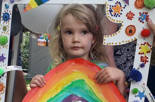 Young girl holding selfie frame and rainbow at Pride