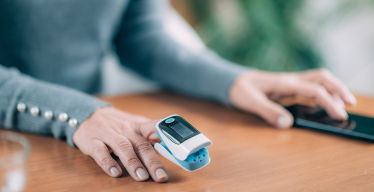 A person with a pulse oximeter on their finger, looking at a mobile phone which collates information from this and other devices.