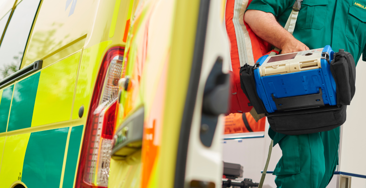 A UK ambulance staff member emerges from the back of an ambulance with his emergency backpack and vital signs monitor.