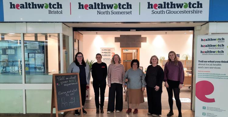 Five members of the Healthwatch team standing at the entrance to their new office under a sign for Healthwatch Bristol, North Somerset and South Gloucestershire.