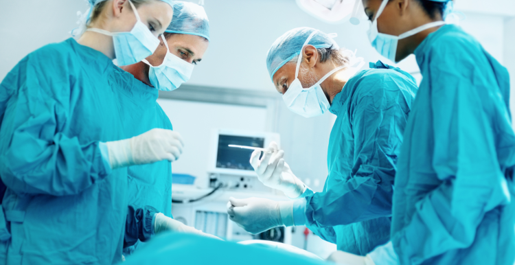 Four medical professionals in surgical scrubs, operating on a patient.