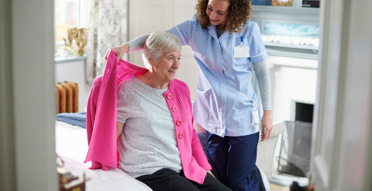 A carer helping an older woman get dressed in her home.