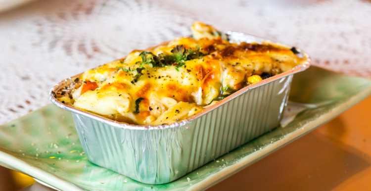 Lasagne ready meal in a foil container on a plate, on a table.