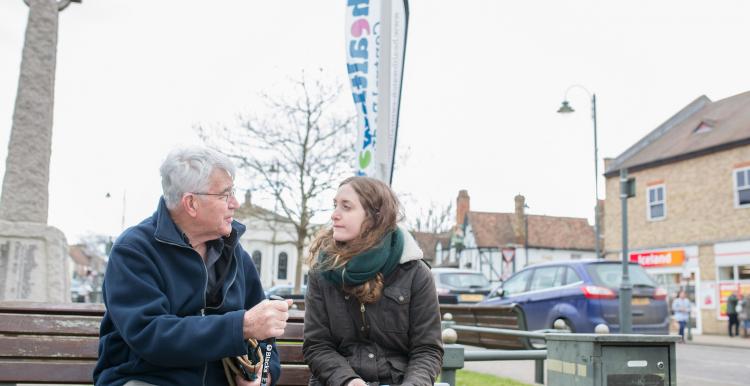 Young woman sitting on a bench talking to an older man