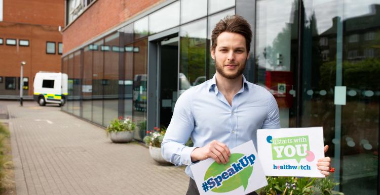 Man outside a hospital holding a #SpeakUp sign