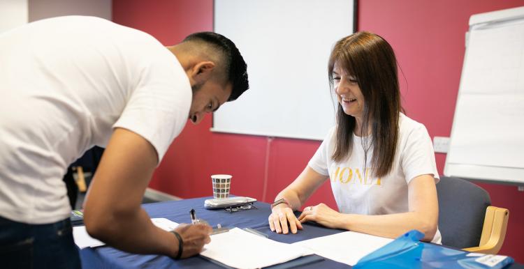 Man filling out a form by a woman sitting at a desk