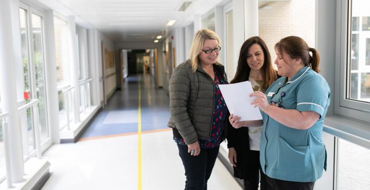 nurse showing files to two ladies in a hospital corridor