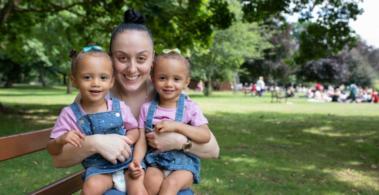 Mum sitting on a park bench with her twins on her lap