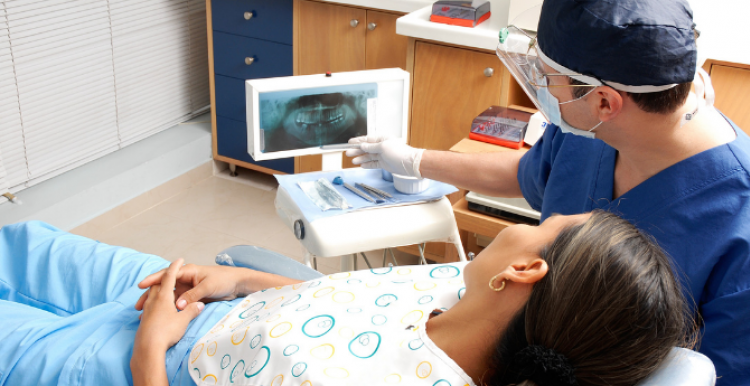 A woman in a dentist's chair, being shown an x-ray by a male dentist