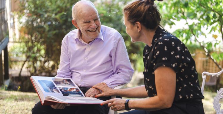 A woman and older man sitting outside and looking at a photo album together