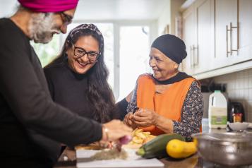 Older Sikh couple receiving help and support while cooking.