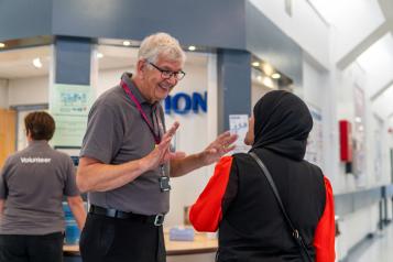 A volunteer talking to a service user or visitor in a hospital corridor.