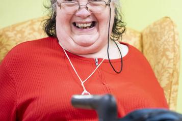 An older woman sitting in an arm chair and smiling. In front of her is a walking frame.