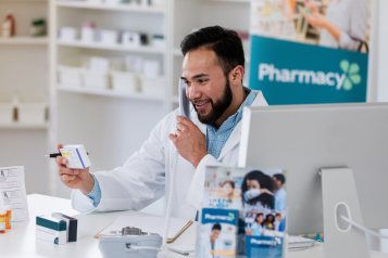 A pharmacist holding a box of medication in a pharmacy while on the phone with a customer.
