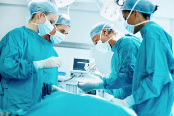 Four medical professionals in surgical scrubs, operating on a patient.