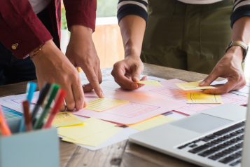 People arranging sticky notes and index cards on a desk.