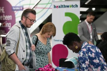 Two people stood looking at a Healthwatch stand at a fair