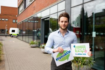 Man outside a hospital holding a #SpeakUp sign