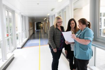 nurse showing files to two ladies in a hospital corridor
