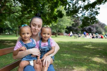Mum sat on a park bench with her two twin daughters