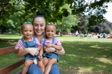 Mum sitting on a park bench with her twins on her lap