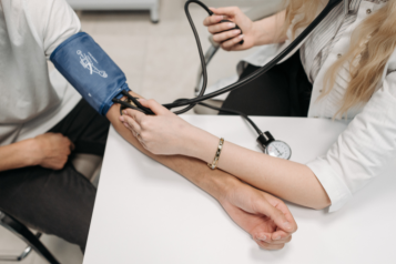 A person wearing a blood pressure cuff getting their blood pressure checked by a medical professional