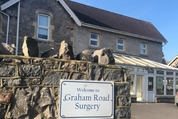A 'Welcome to Graham Road Surgery' sign with the surgery in the background