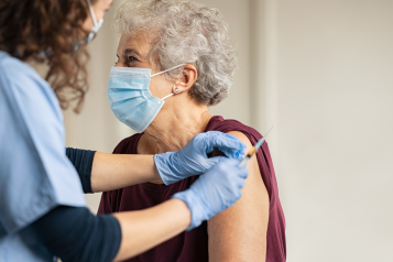 An older woman wearing a face mask receiving a vaccine