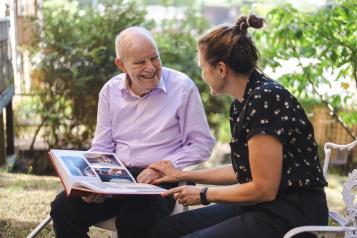 A woman and older man sitting outside and looking at a photo album together