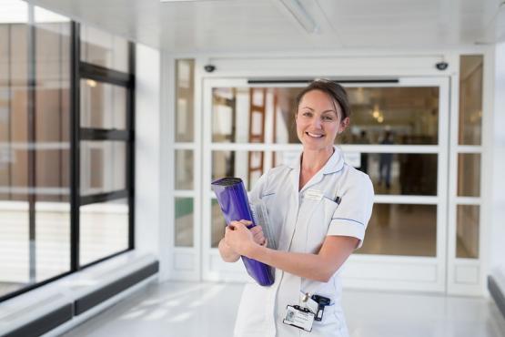 A nurse in a white uniform smiling in a hospital corridor