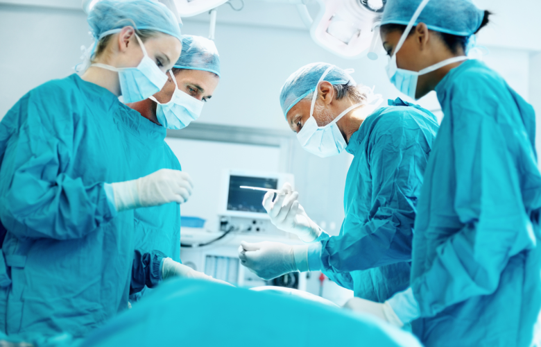 Four medical professionals in surgical scrubs, operating on a patient.