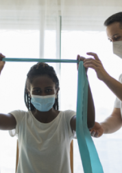 A medical professional helping a woman hold a piece of fabric between her hands, with her arms raised over her head