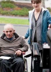 Man in a wheelchair being helped into a bus